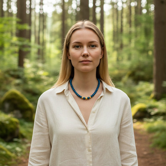 Eine Halskette aus Perlen aus blauem Achat-Geode von Sinnikäs mit goldenen Akzentperlen, getragen von einer Frau in einem Leinenhemd im Wald.