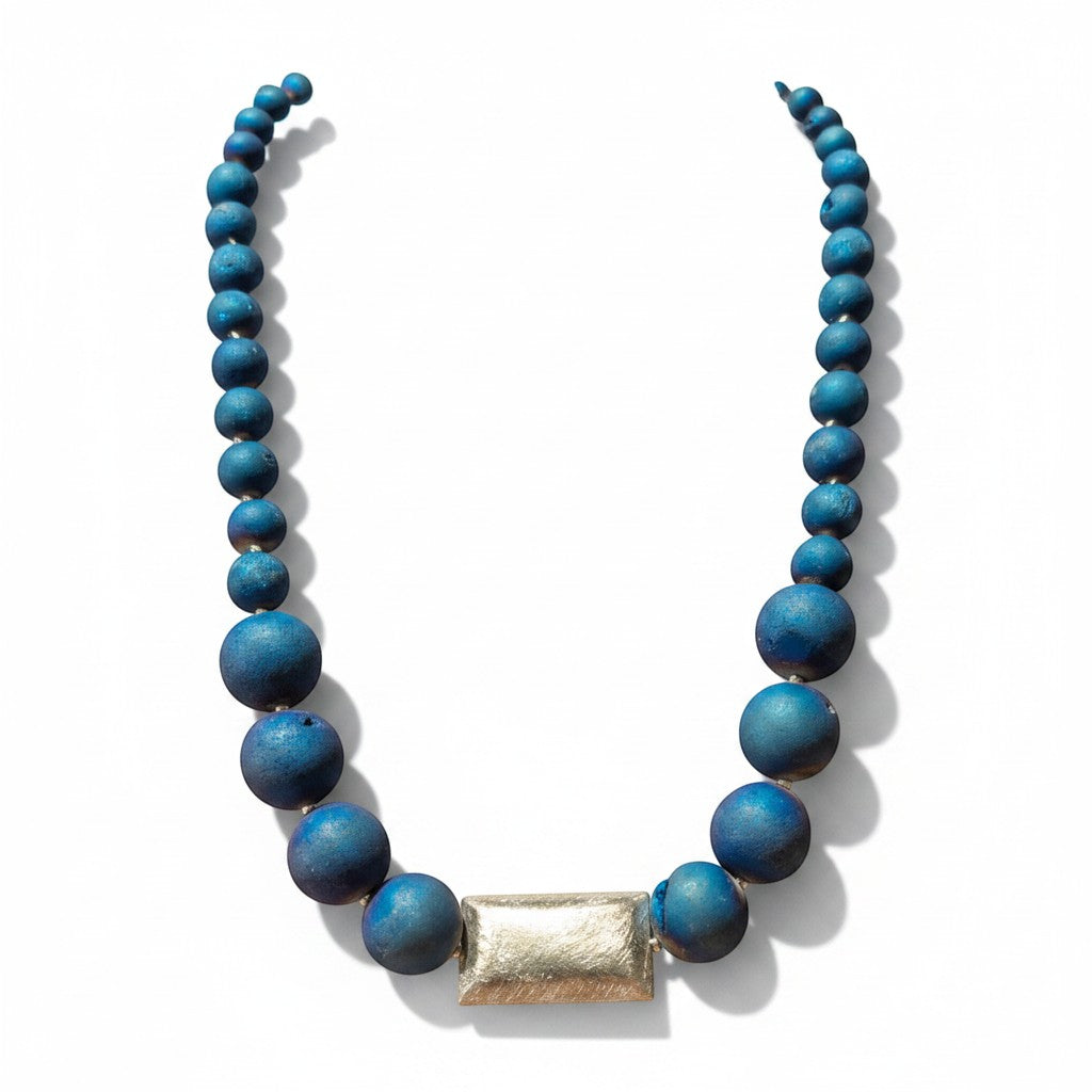 Eine elegante Halskette aus blauen Geoden-Achatperlen mit einem rechteckigen Mittelstück aus 925er Silber. Sie zeichnet sich durch unterschiedlich große Perlen und eine strukturierte Oberfläche aus.