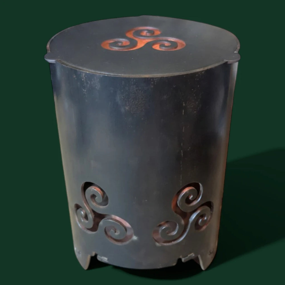 Keltische Sinnikäs Gartenfackel aus dunklem Stahl mit aufgesetztem Metalldeckel und eingearbeitetem Triskele-Symbol vor einem dunkelgrünen Hintergrund.
