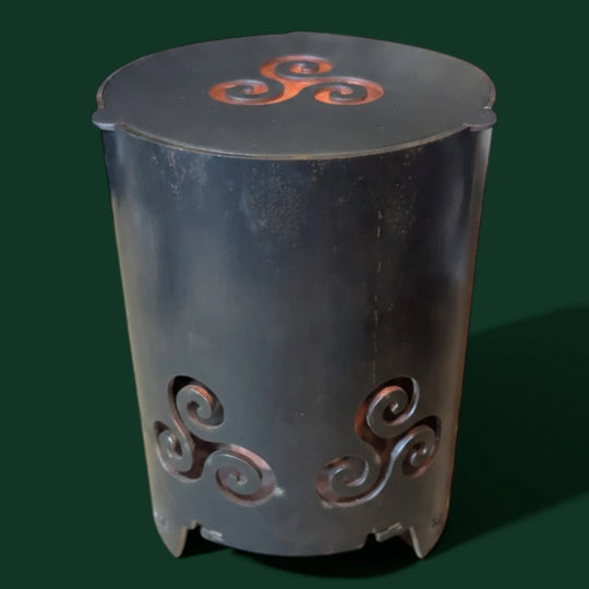 Keltische Sinnikäs Gartenfackel aus dunklem Stahl mit aufgesetztem Metalldeckel und eingearbeitetem Triskele-Symbol vor einem dunkelgrünen Hintergrund.