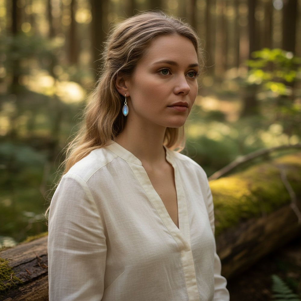 Sinnikäs Mondstein Ohrhänger aus 925er Silber, tropfenförmig, milchig-transluzent, an einer jungen Frau mit blonden Haaren im Wald getragen.