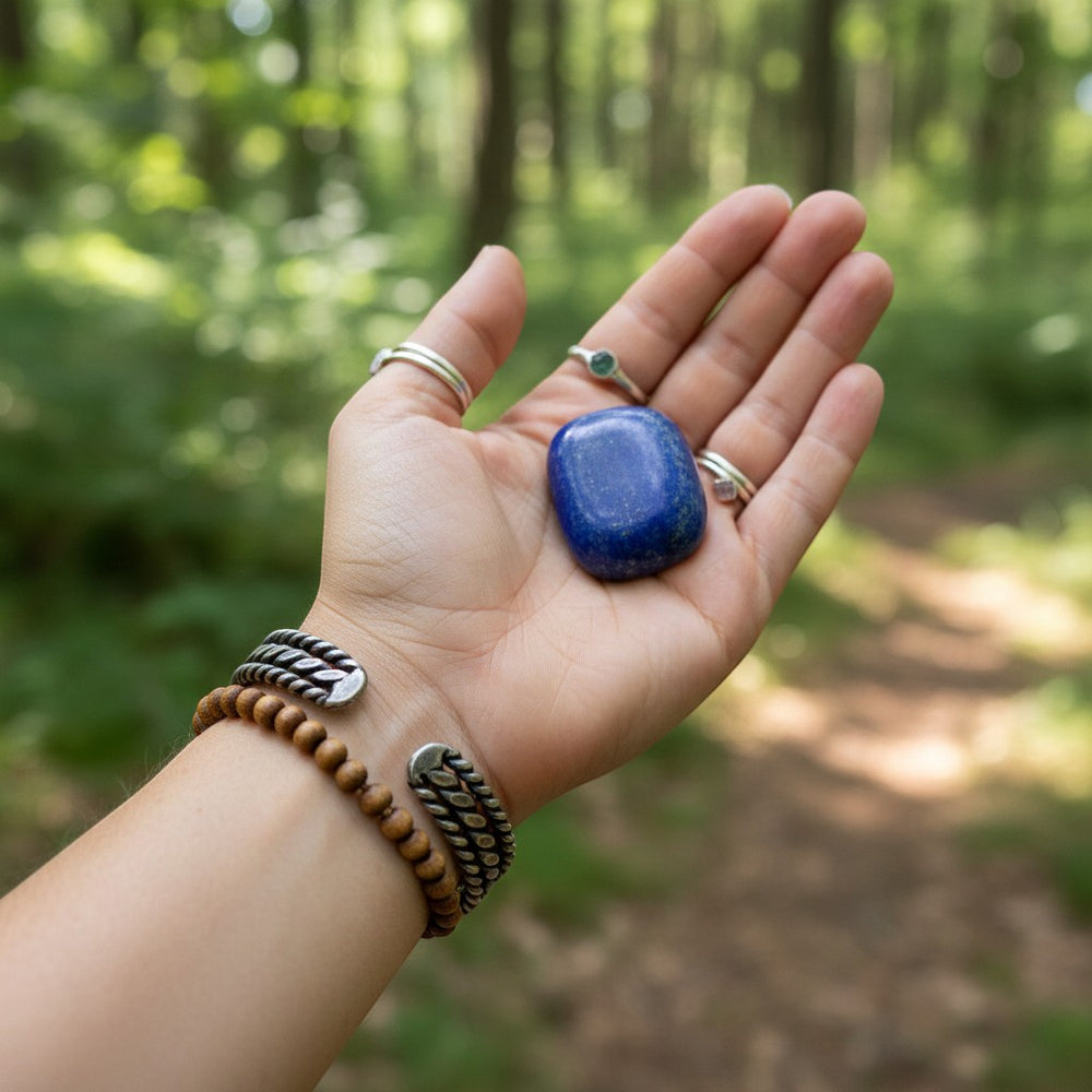 Sinnikäs silberner Armreif mit geflochtenem Muster und Holzperlenarmband, gehalten in einer Hand mit einem blauen Lapislazuli-Stein.