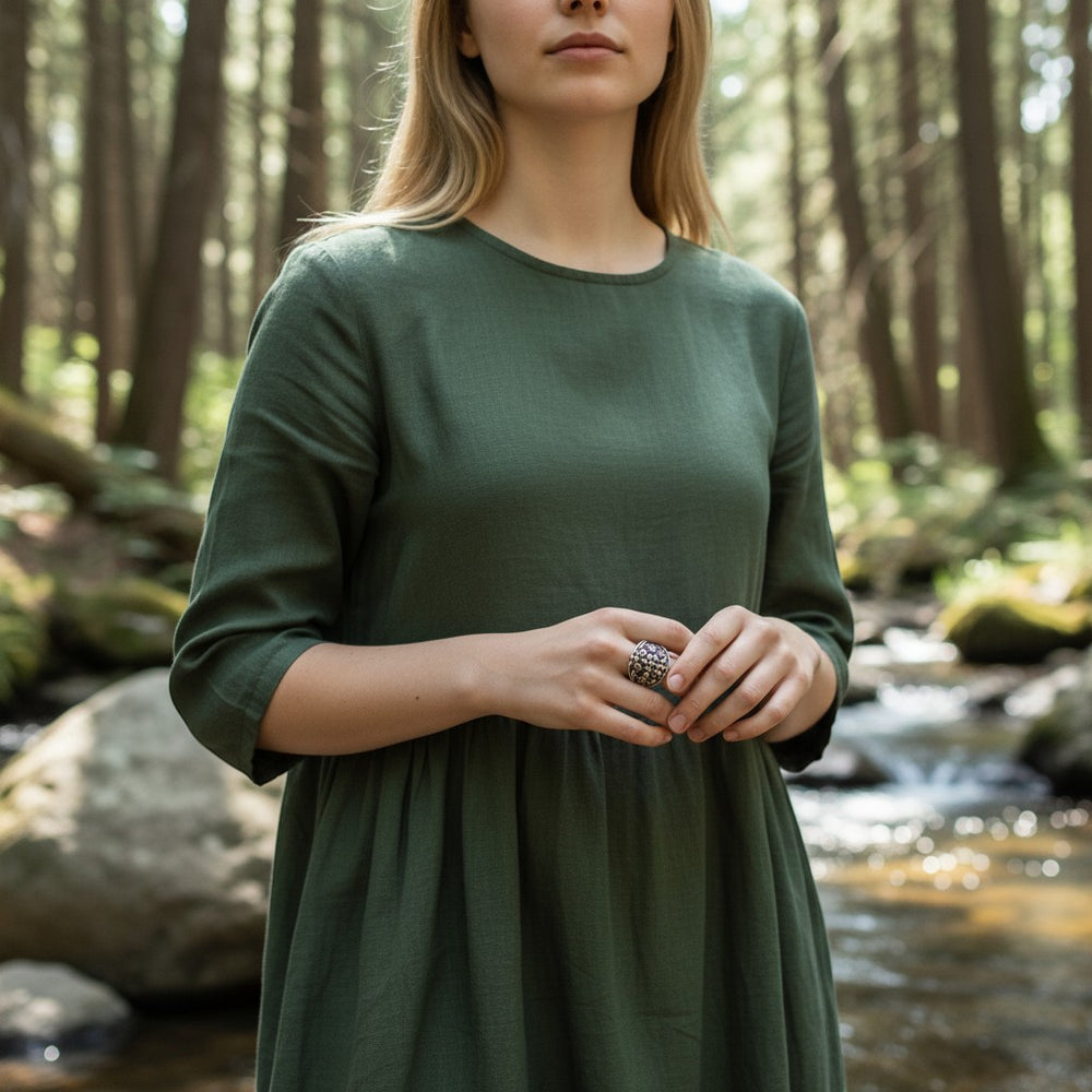 Sinnikäs silberner Ring mit Blumenmuster, kunstvoll und asymmetrisch, getragen von einem Model in einem grünen Kleid im Wald.