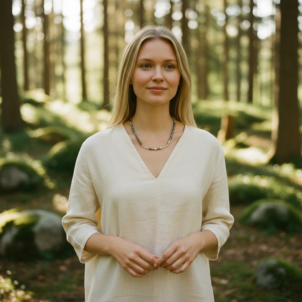 Sinnikäs Halskette mit facettierten Siliziumperlen und diamantierter 925er Silberkugel, getragen von einem Model in einem cremefarbenen Leinenkleid im Wald.