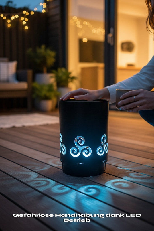 Sinnikäs Gartenfackel aus schwarzem Stahl mit Triskele-Ausschnitten, die Lichtmuster projizieren. Mit LED-Leuchte.